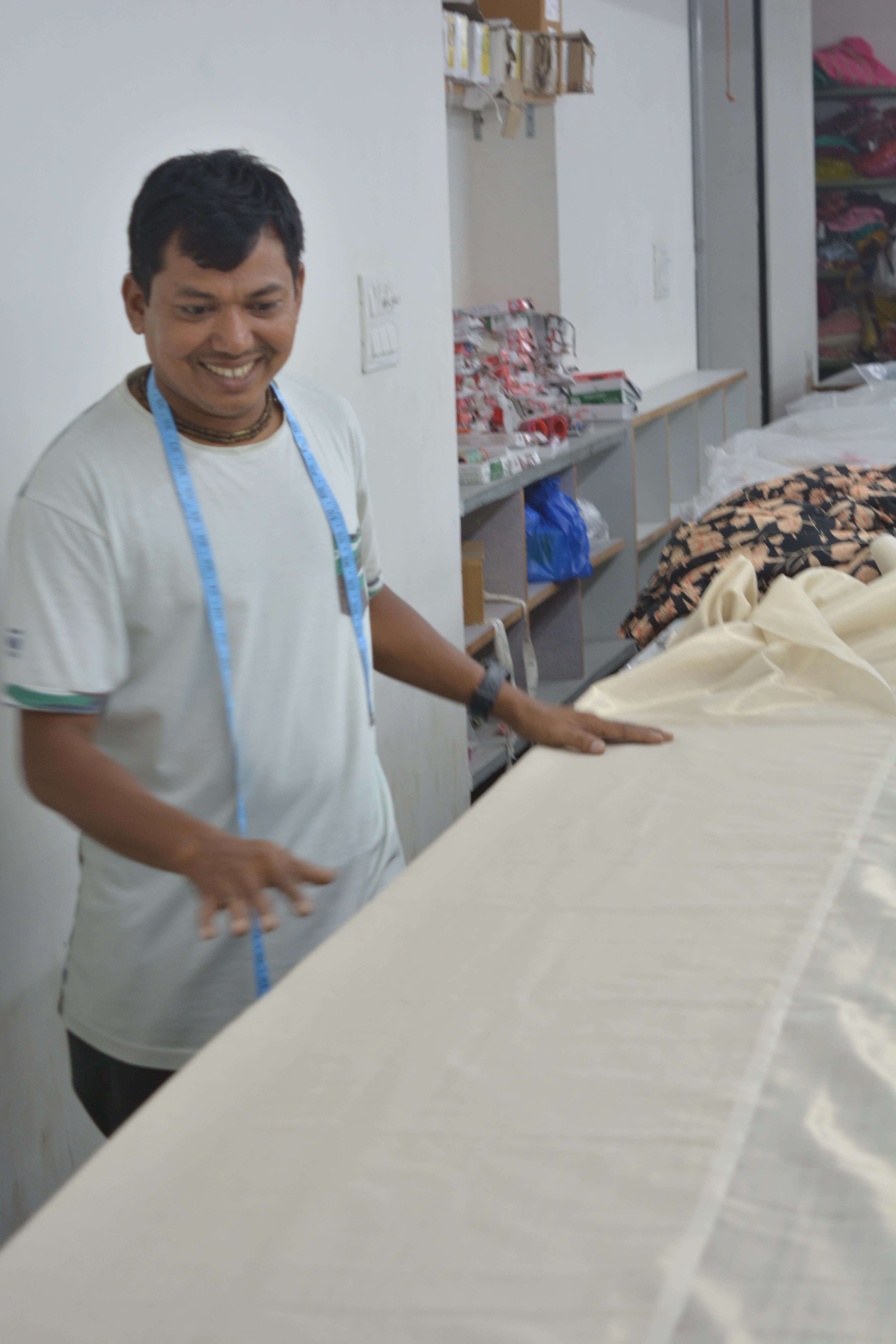 Cutter with tape measure smiling at the cutting table, cream fabric laid out