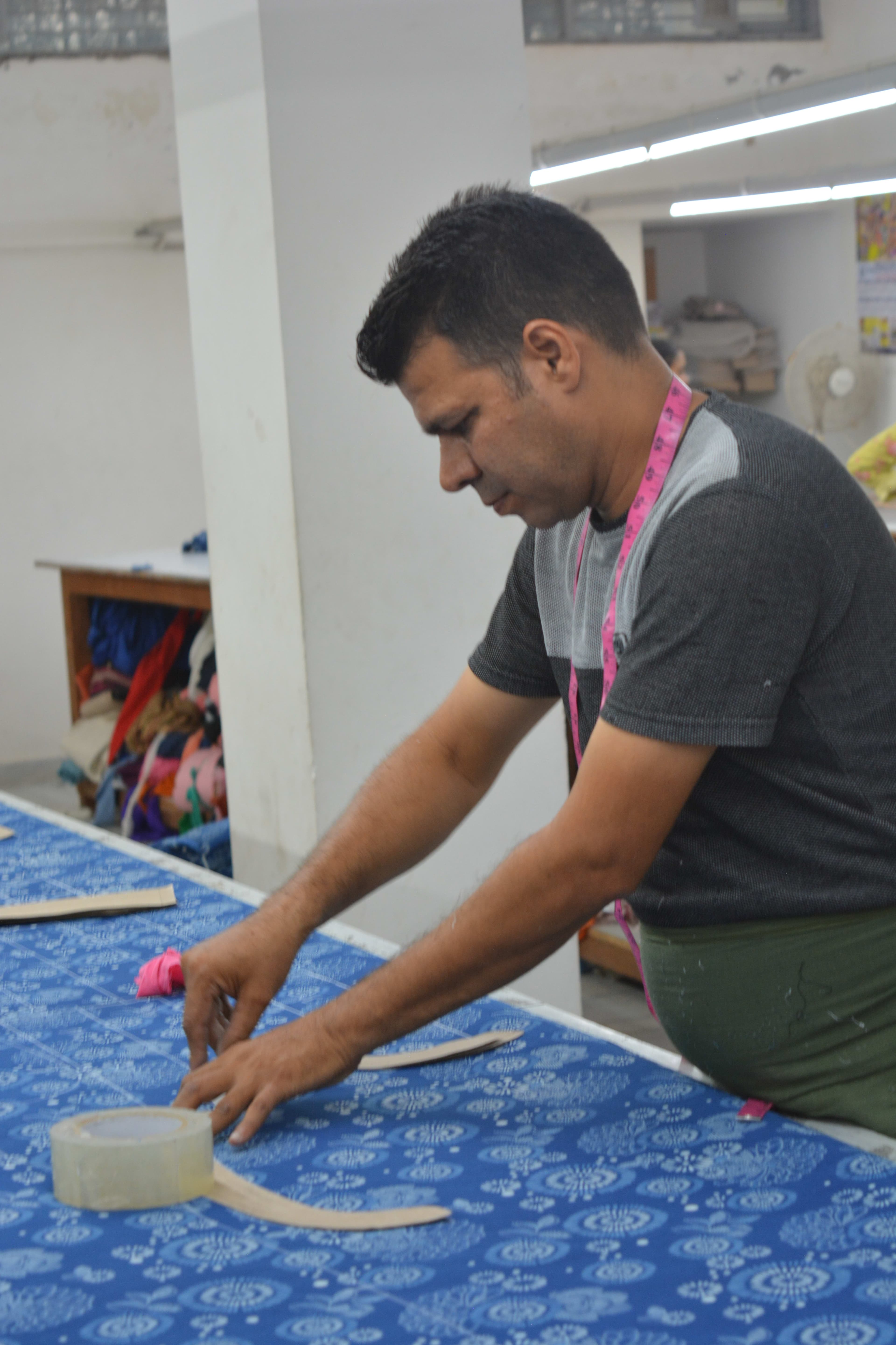 Cutter placing paper pattern pieces on blue block-printed fabric, tape measure visible