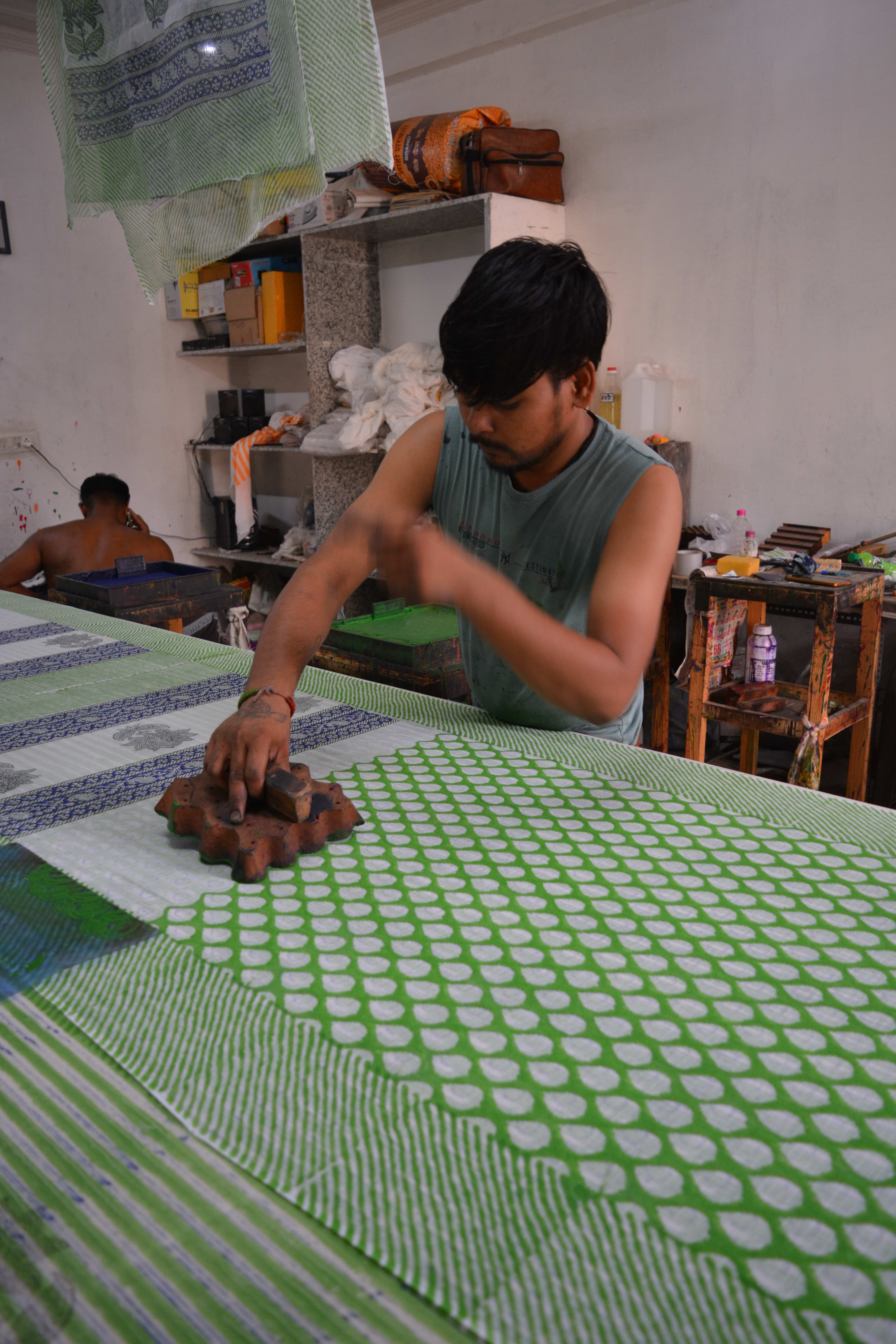 Artisan pressing a block print onto green fabric stretched across a long printing table